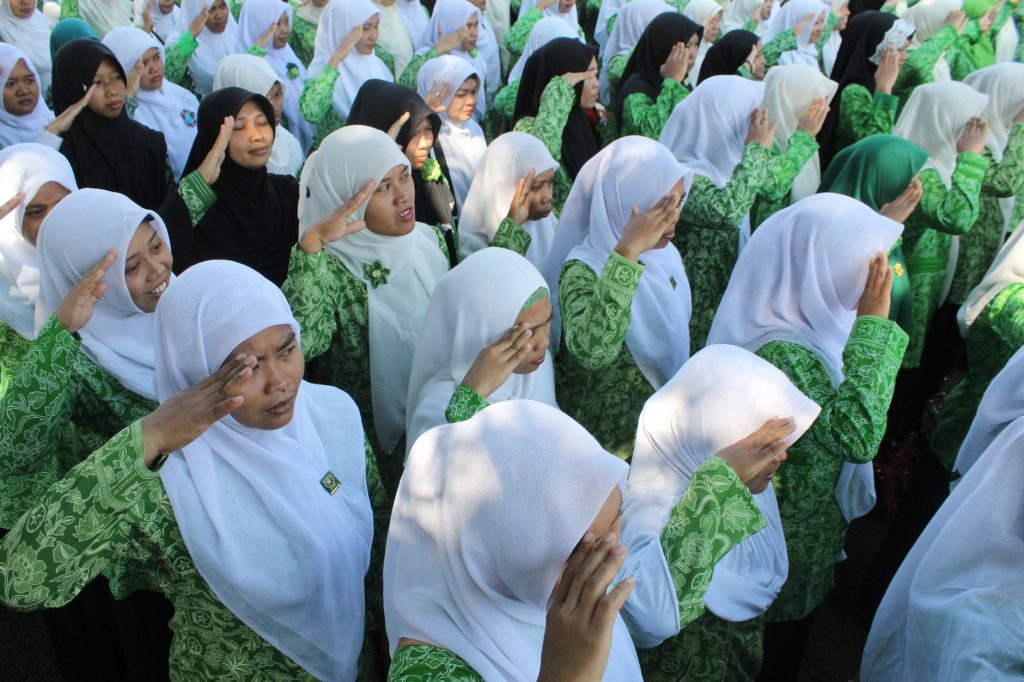 A group of Muslim women in traditional attire participating in a ceremonial salute outdoors in Indonesia.