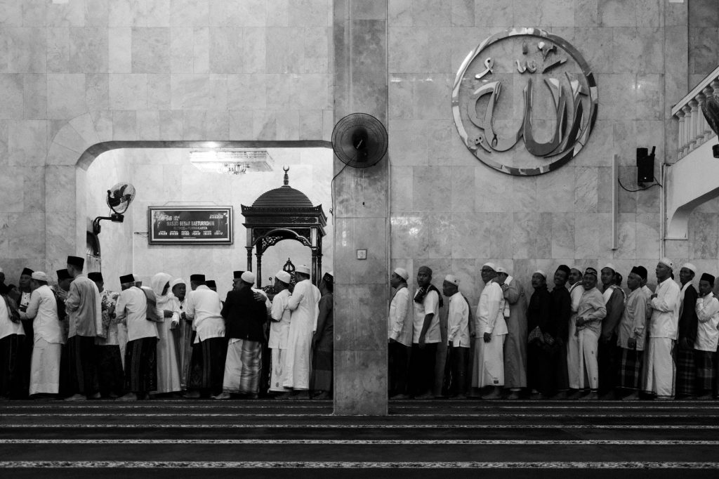 A group of people gathered inside a mosque for a cultural or religious event in black and white.