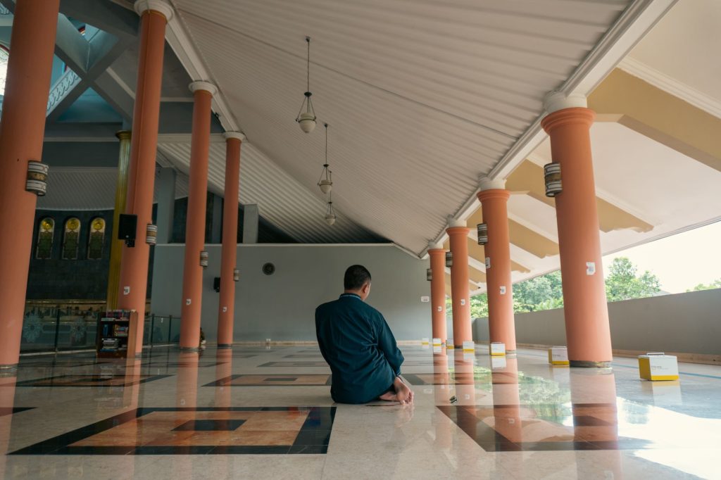 Man in serene prayer in Yogyakarta mosque interior, showcasing architectural elegance.