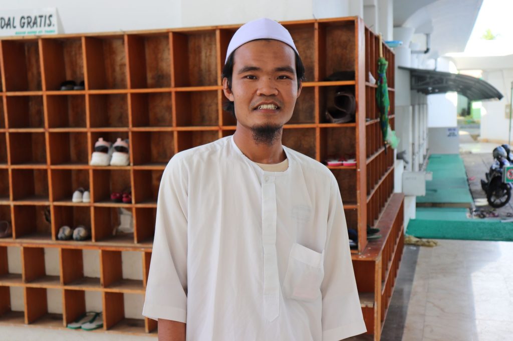 A man in a white thobe smiles at a mosque in Bengkulu, Indonesia.